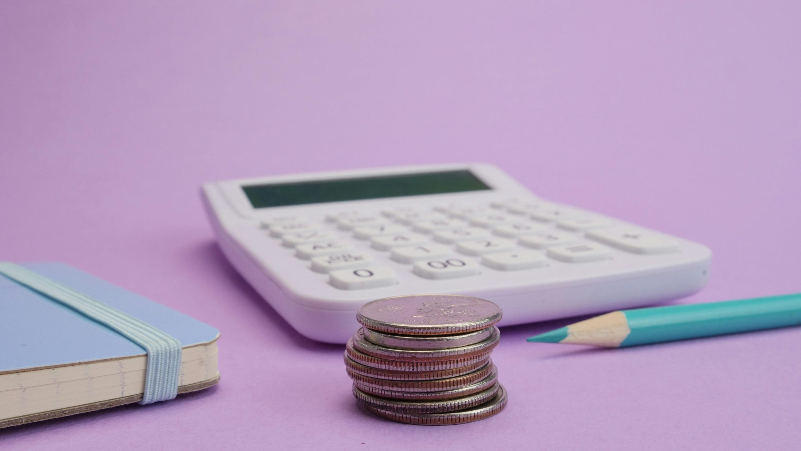 calculator, pencil, and stacked coins on a purple surface