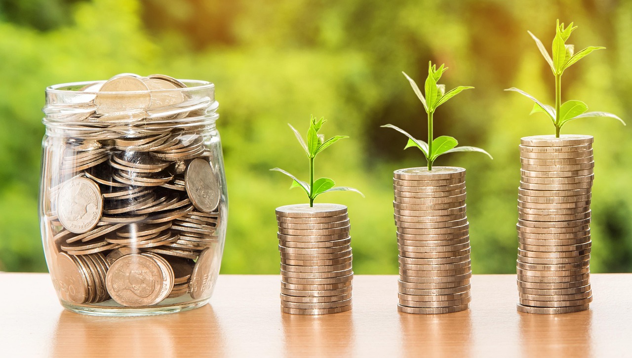 jar filled with coins and three stacks of coins with sprouts on top
